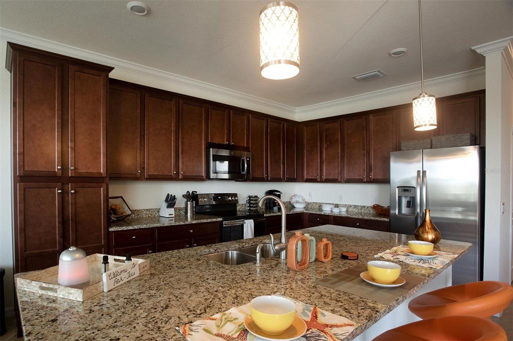 A kitchen with dark wood cabinets, granite countertops, a center island, and stainless steel appliances — 17108 VARDON TERRACE UNIT 401, BRADENTON, FL