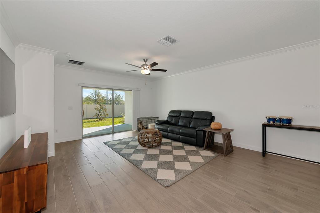 A living room with light wood-look tile flooring, a black leather sofa, and sliding glass doors — 17322 HOLLY WELL AVENUE, WIMAUMA, FL
