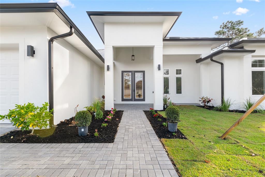 A modern white house exterior features a paved walkway leading to a double front door — 45 VINCA STREET, HOMOSASSA, FL