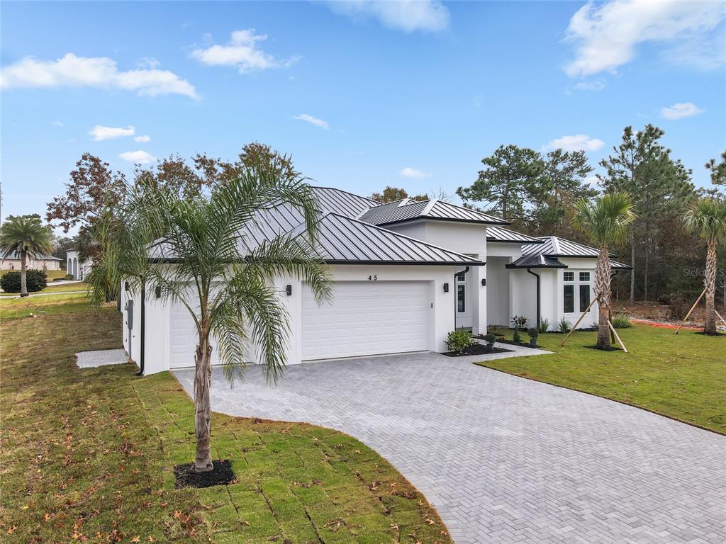 A white single-story house with a metal roof and a paved driveway sits on a lawn — 45 VINCA STREET, HOMOSASSA, FL
