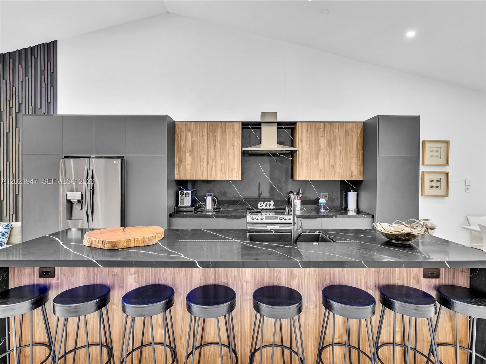 A modern kitchen features a black marble island with bar seating and wood-accented cabinetry — 500 NE 199th Ter # 7J, Miami FL 33179, MIAMI, FL