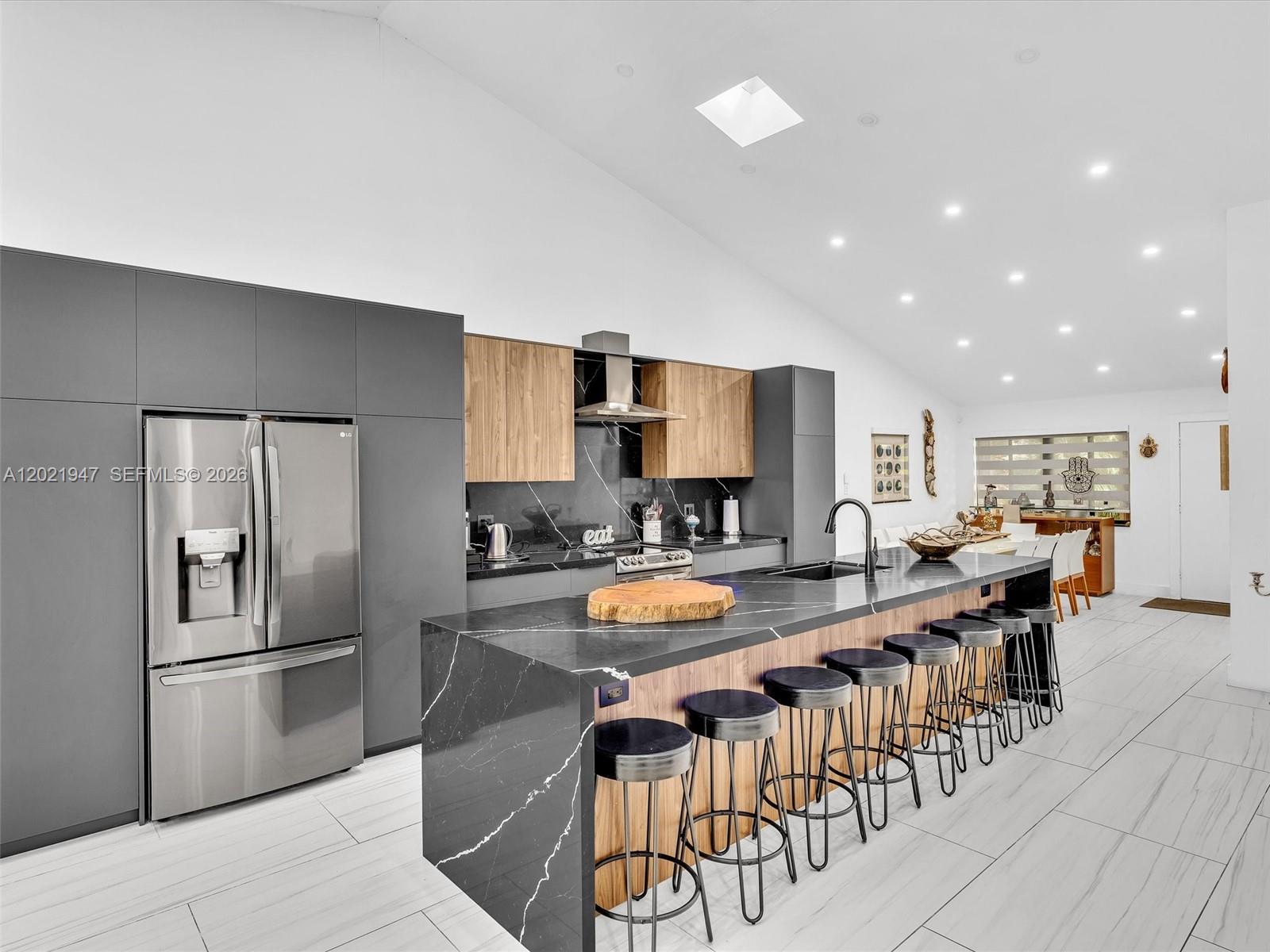 A modern kitchen features dark gray cabinetry, a black marble island, and wood-toned accents — 500 NE 199th Ter # 7J, Miami FL 33179, MIAMI, FL