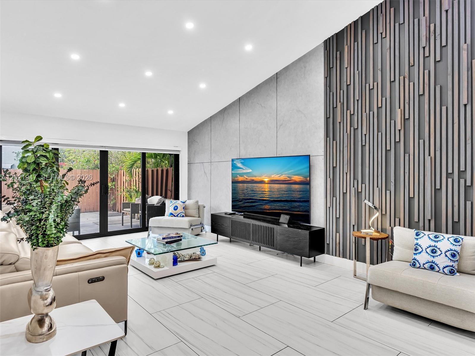A modern living room features a concrete accent wall, wood slat paneling, and sliding glass doors — 500 NE 199th Ter # 7J, Miami FL 33179, MIAMI, FL