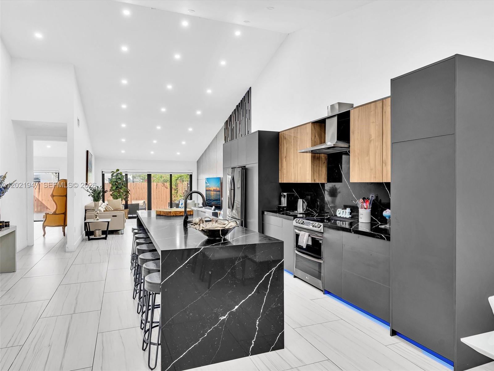 A modern kitchen features a large black marble island, dark cabinetry, and wood-toned upper cabinets — 500 NE 199th Ter # 7J, Miami FL 33179, MIAMI, FL