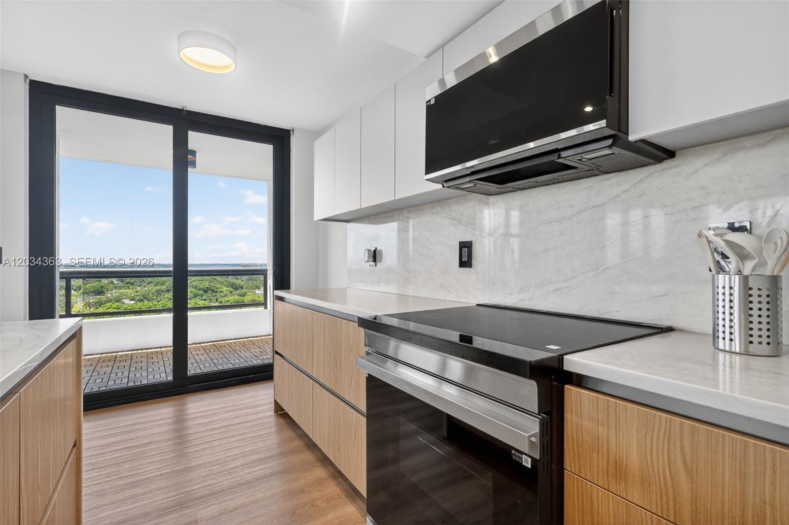 A modern kitchen features light wood cabinets, white countertops, and a balcony with a view — 2555 Collins Ave # 1812, Miami Beach FL 33140, MIAMI BEACH, FL