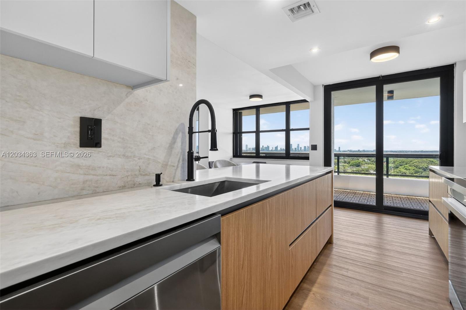 A modern kitchen features wood-toned cabinetry, a white stone countertop, and a balcony with views — 2555 Collins Ave # 1812, Miami Beach FL 33140, MIAMI BEACH, FL