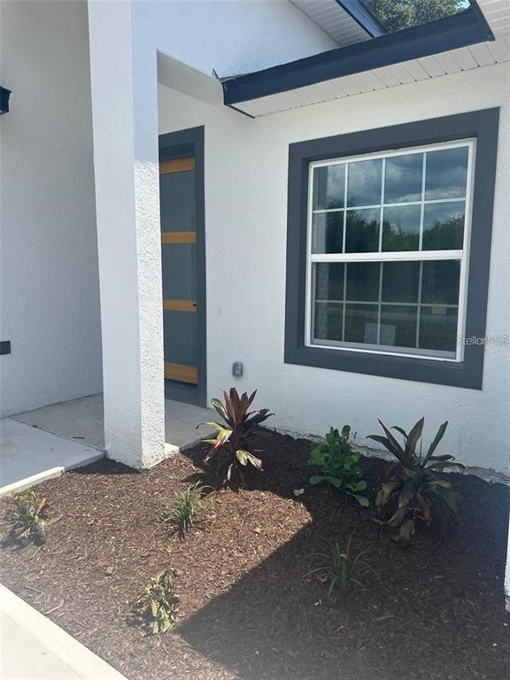 A white stucco house exterior features a dark-trimmed window and a modern wood-accented front door — 5842 SW 154TH LANE ROAD, OCALA, FL