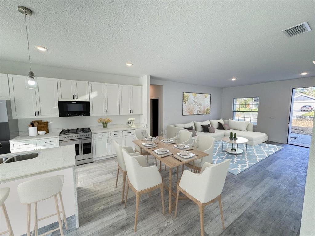 An open-concept kitchen, dining area, and living room feature white cabinetry and light wood flooring — 5842 SW 154TH LANE ROAD, OCALA, FL