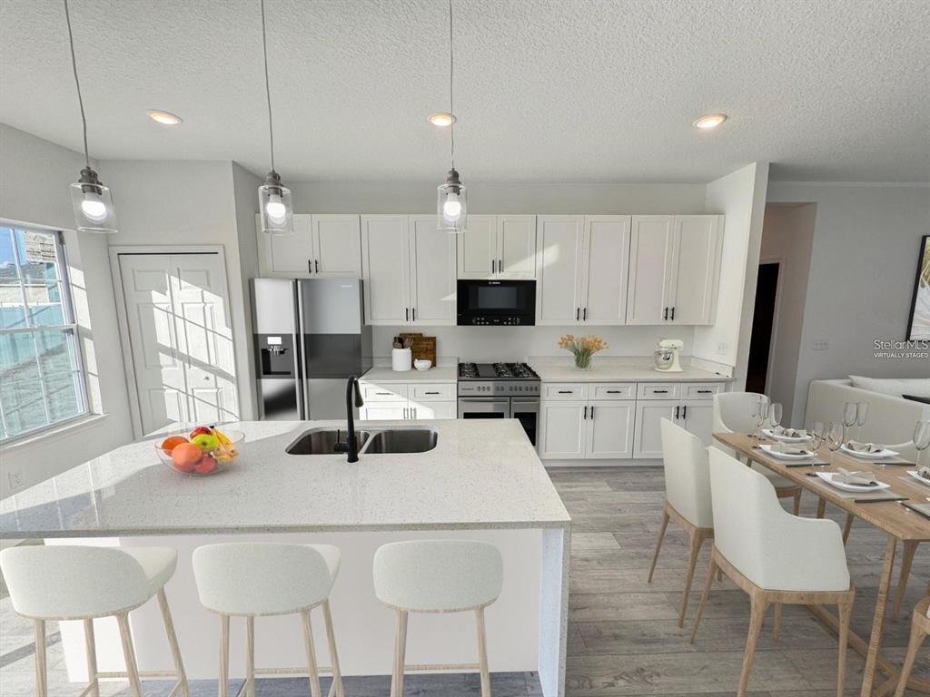 A modern kitchen features white cabinetry, a quartz island with a sink, and stainless appliances — 5842 SW 154TH LANE ROAD, OCALA, FL