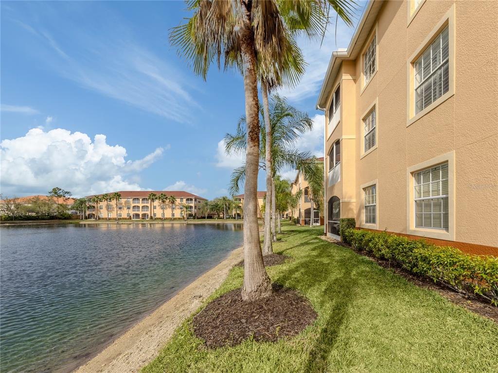 A multi-story apartment building sits beside a lake with palm trees and green grass — 1731 AUBURN LAKES DRIVE UNIT 24, VENICE, FL