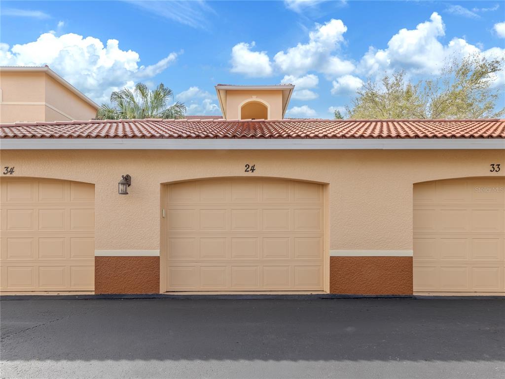 A row of three beige garage doors with a tiled roof under a blue sky — 1731 AUBURN LAKES DRIVE UNIT 24, VENICE, FL