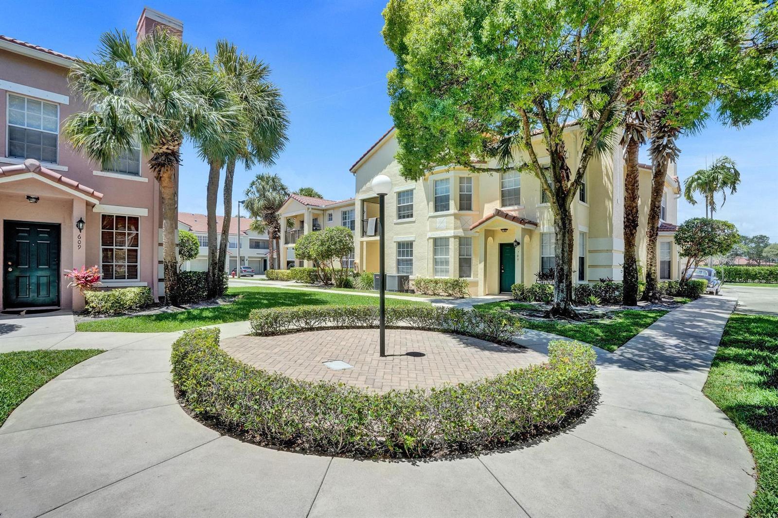 An exterior view of two multi-story apartment buildings with a circular brick courtyard and landscaping — 708 Belmont Place, Boynton Beach FL 33436, BOYNTON BEACH, FL