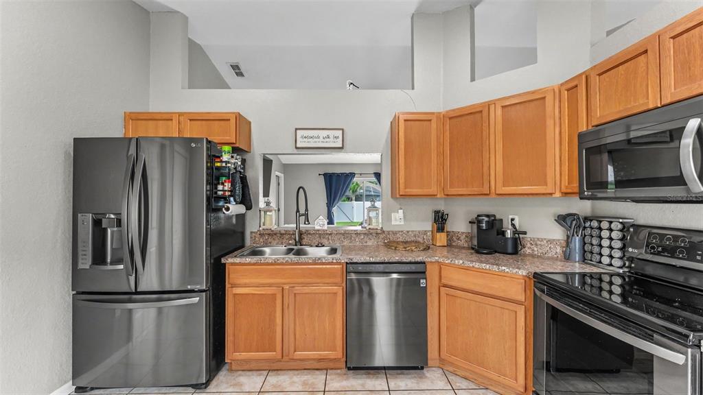 A kitchen features wood cabinets, stainless steel appliances, and a pass-through window to another room — 1320 NORMANDY HEIGHTS CIRCLE, WINTER HAVEN, FL