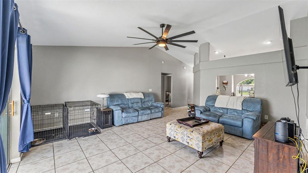 A living room features tile flooring, two blue sofas, a patterned ottoman, and dog crates — 1320 NORMANDY HEIGHTS CIRCLE, WINTER HAVEN, FL