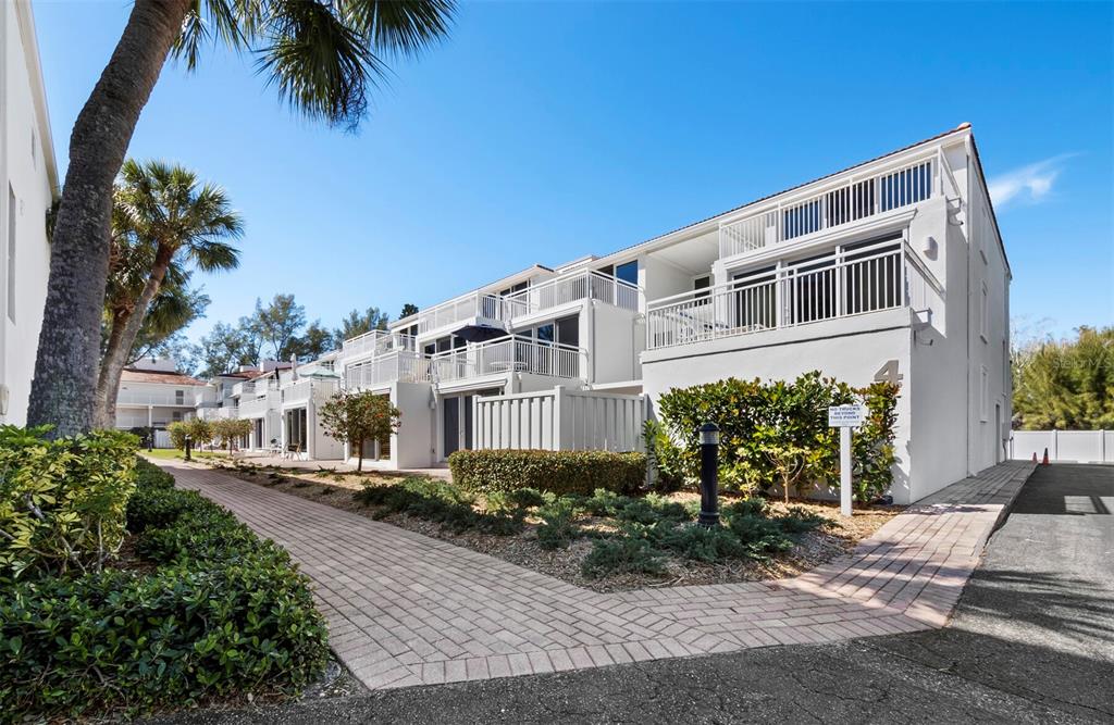A multi-story white residential building with balconies and a brick walkway in front — 5055 GULF OF MEXICO DRIVE UNIT 421, LONGBOAT KEY, FL