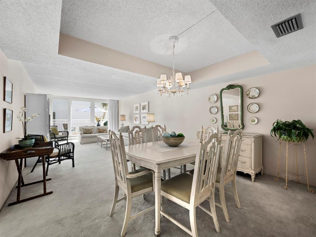 A dining area with a chandelier and table set sits before a carpeted living room — 5055 GULF OF MEXICO DRIVE UNIT 421, LONGBOAT KEY, FL