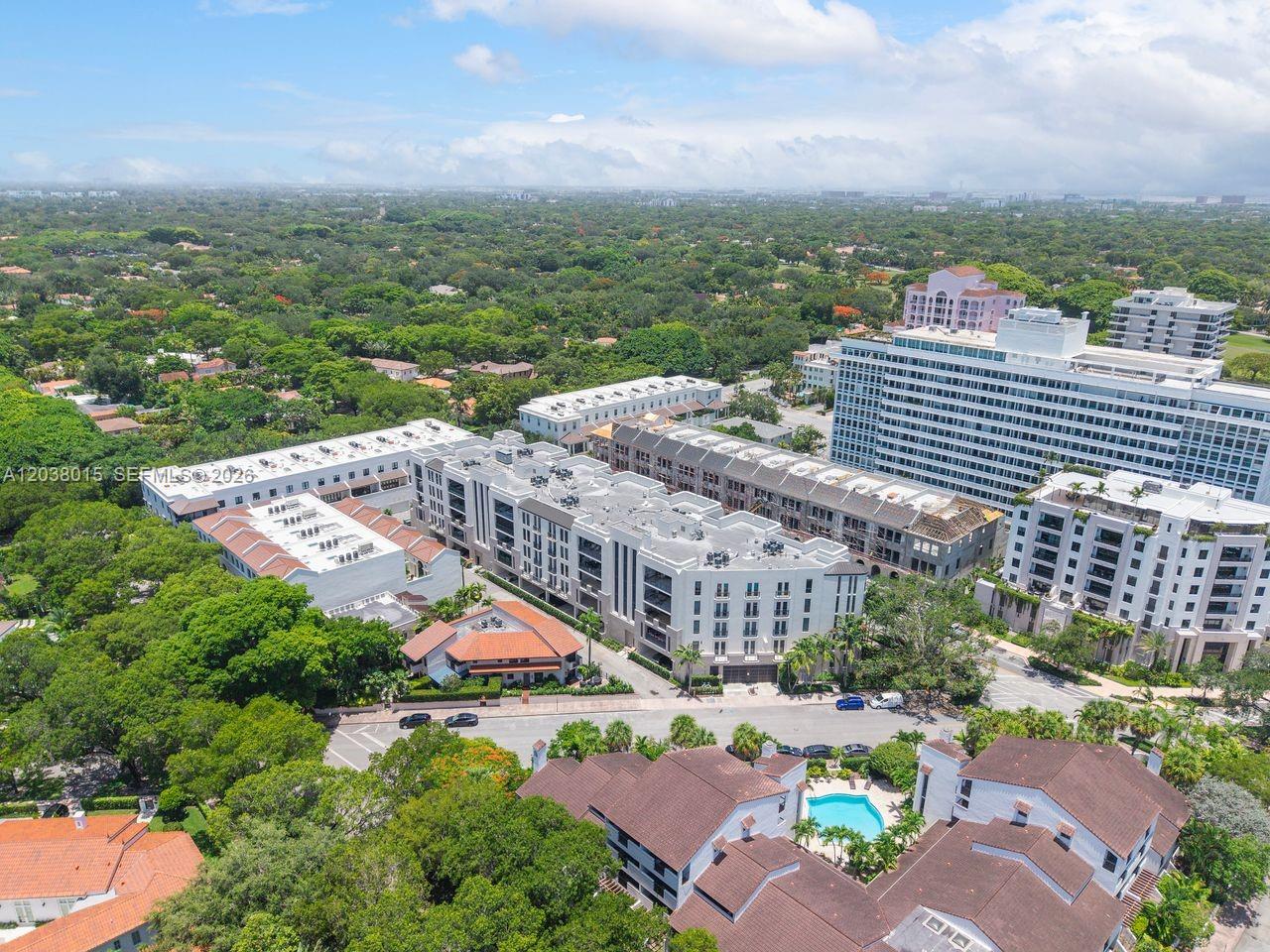 An aerial view shows a multi-story apartment complex surrounded by lush trees and nearby buildings — 718 Valencia Ave # 403, Coral Gables FL 33134, CORAL GABLES, FL