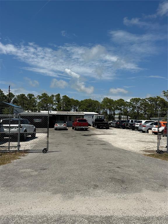 A gravel parking lot leads to a single-story commercial building surrounded by a chain-link fence — 54 HARVARD STREET, ENGLEWOOD, FL