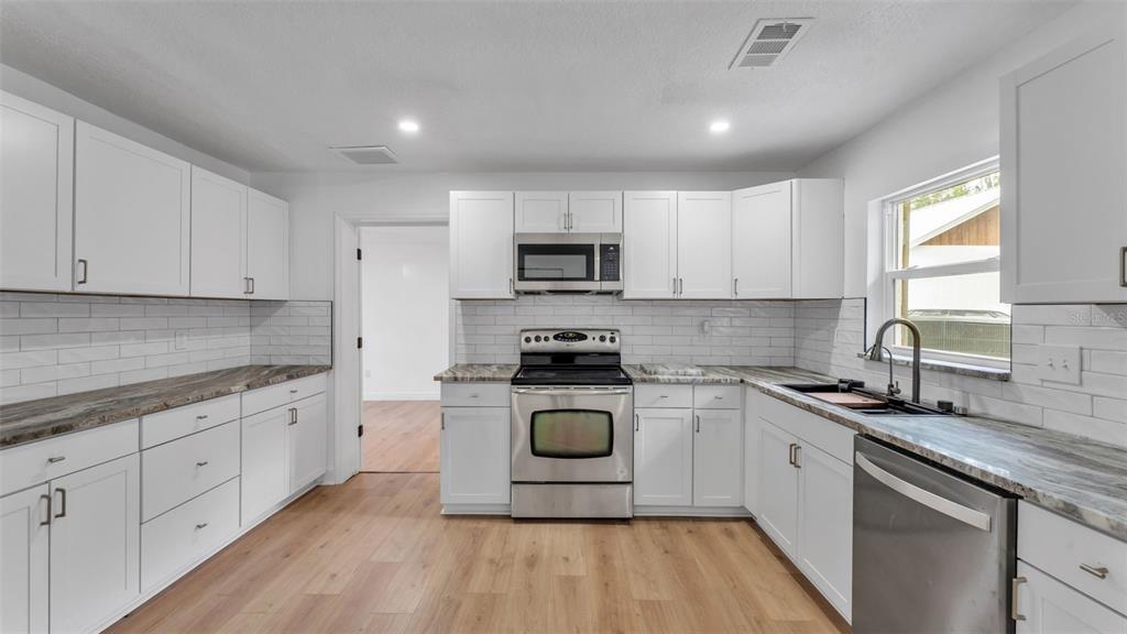 A kitchen with white cabinets, stainless steel appliances, wood-look flooring, and a subway tile backsplash — 3781 N HIAWATHA TERRACE, CRYSTAL RIVER, FL
