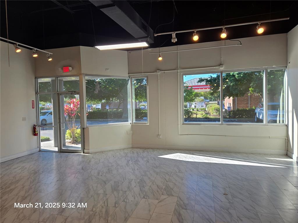 An empty commercial space features marble-look tile flooring, large windows, and exposed ceiling lighting — 7901 KINGSPOINTE PARKWAY UNIT 23, ORLANDO, FL