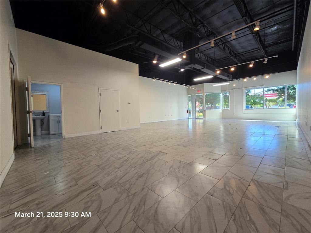An open commercial space features white walls, marble-look tile flooring, and exposed black ceilings — 7901 KINGSPOINTE PARKWAY UNIT 23, ORLANDO, FL