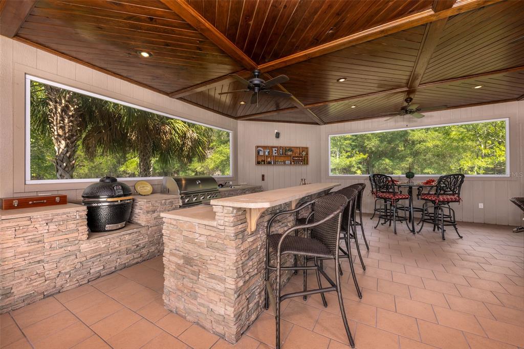 An outdoor kitchen features a stone bar, grill, ceramic cooker, and a wood-paneled ceiling — 19103 NW 72ND AVENUE, ALACHUA, FL