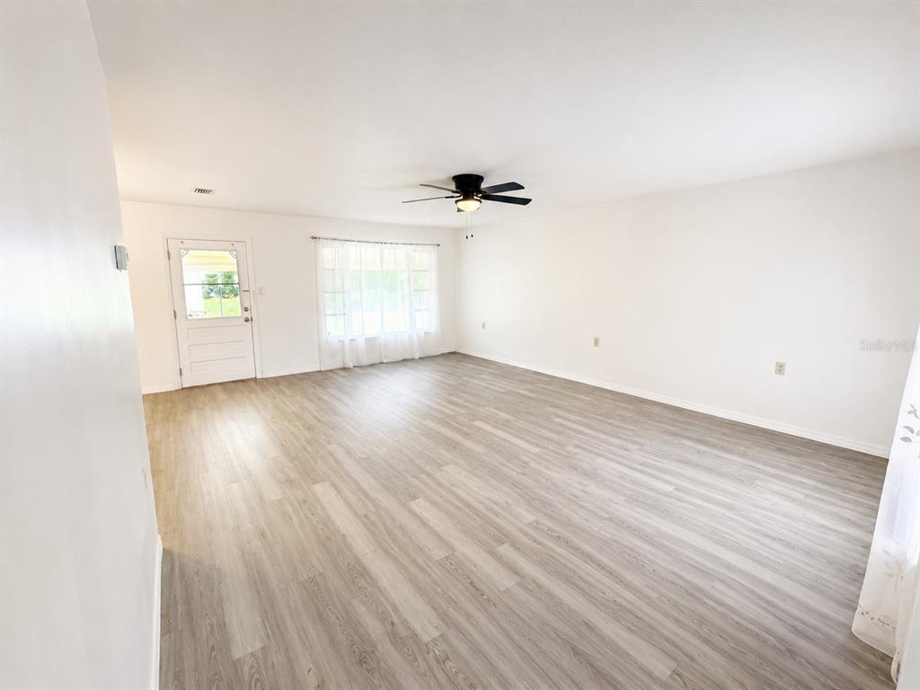 A bright, empty living room features light wood-look flooring, white walls, and a ceiling fan — 21136 SW HONEYSUCKLE STREET, DUNNELLON, FL