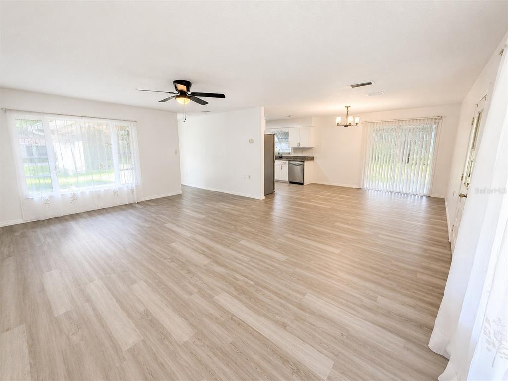 An open-concept living and dining area features light wood-look flooring and a white kitchen — 21136 SW HONEYSUCKLE STREET, DUNNELLON, FL