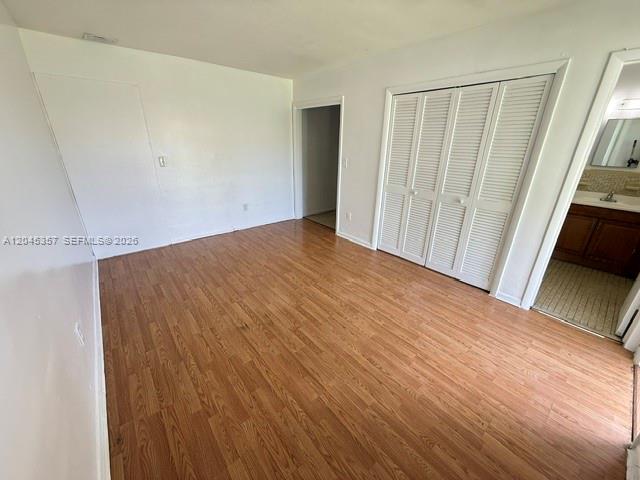 A bedroom features wood-look flooring, white walls, a closet with louvered doors, and an attached bathroom — 5946 Mckinley St # B, Hollywood FL 33021, HOLLYWOOD, FL