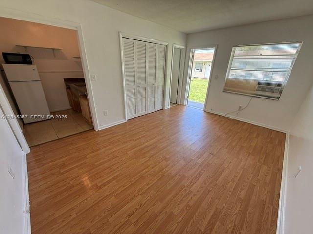 A room with wood-look flooring, a white refrigerator, louvered closet doors, and an exterior door — 5946 Mckinley St # B, Hollywood FL 33021, HOLLYWOOD, FL