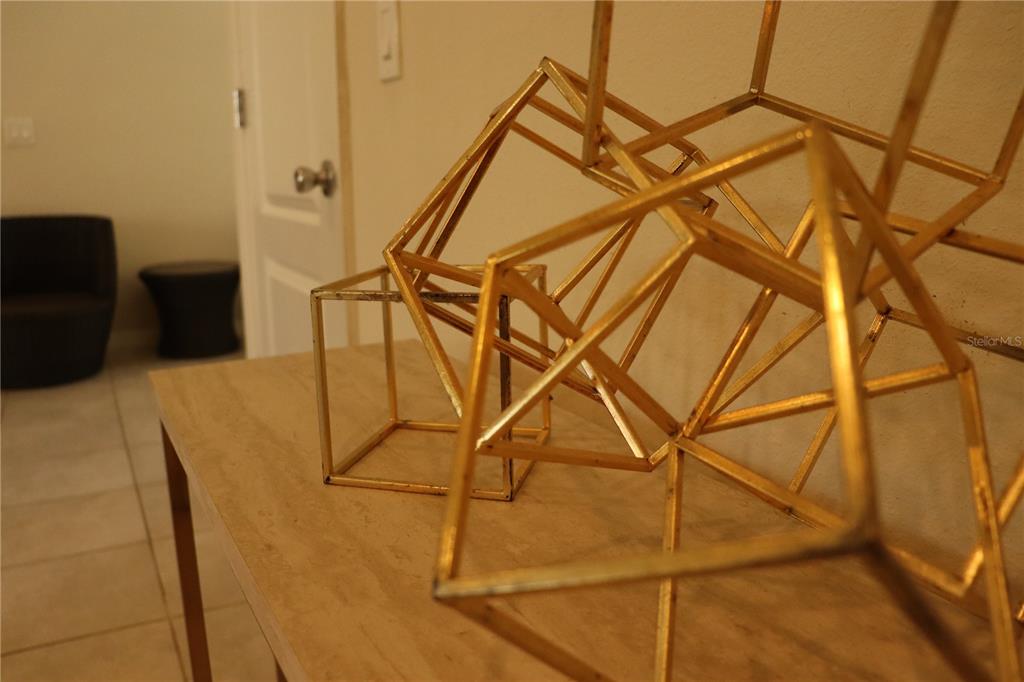 A gold geometric sculpture sits on a wooden table in a room with tiled floors — 8926 ZURICH LANE, KISSIMMEE, FL