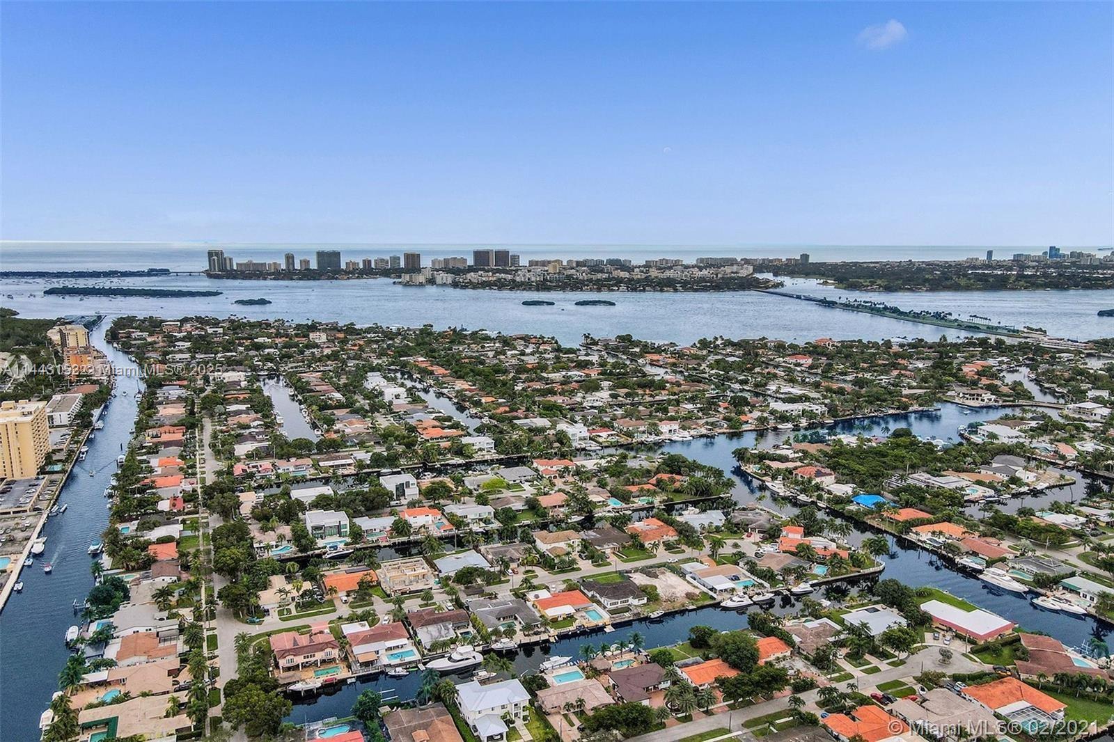 An aerial view shows a residential neighborhood with canals, boat docks, and distant coastal buildings — 13499 Biscayne Blvd # 1513, North Miami FL 33181, NORTH MIAMI, FL