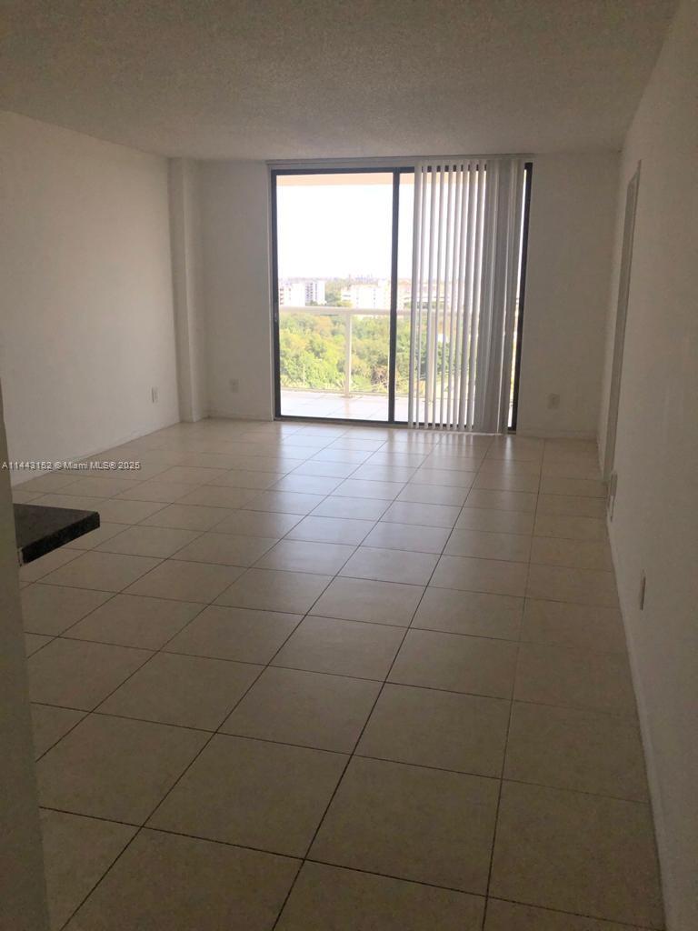 An empty room with light-colored tile flooring and a sliding glass door to a balcony — 13499 Biscayne Blvd # 1513, North Miami FL 33181, NORTH MIAMI, FL