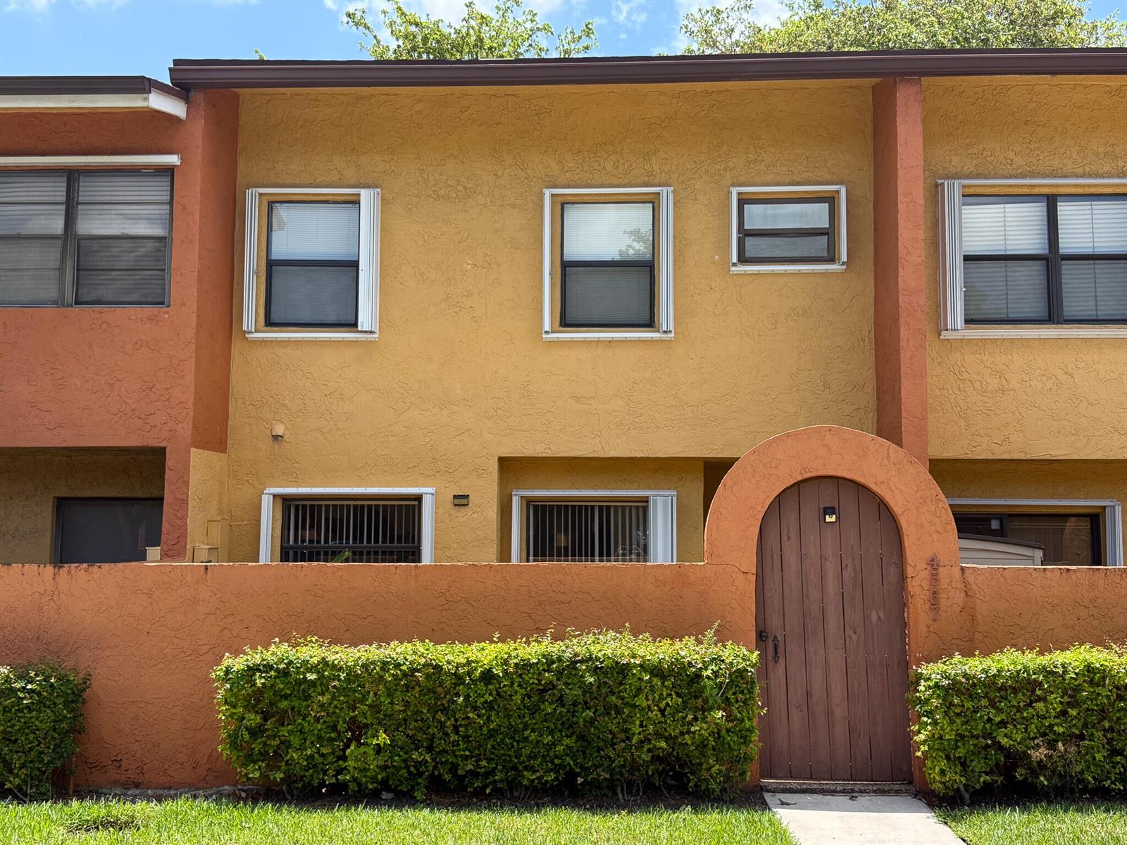 A two-story townhouse exterior features yellow stucco walls, an arched wooden gate, and hedges — 4567 NW 90th Avenue, Sunrise FL 33351, SUNRISE, FL