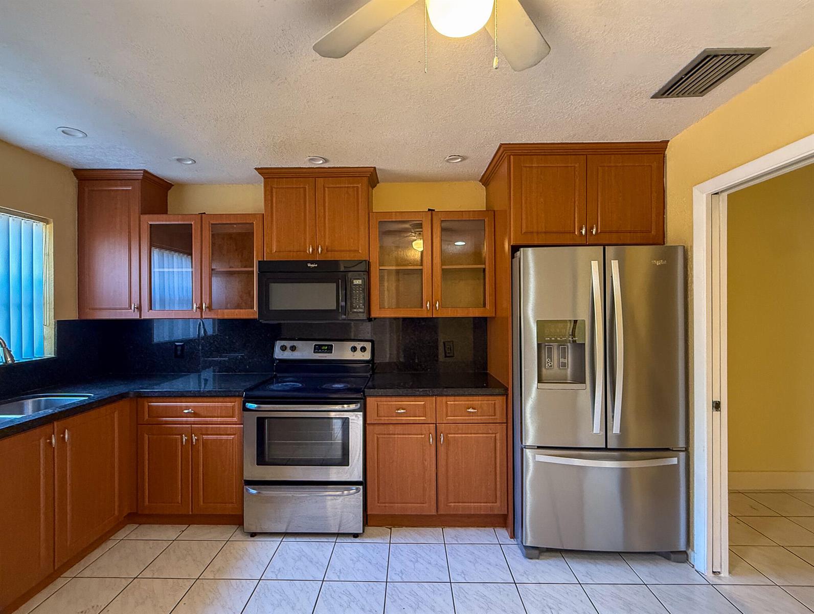 A kitchen features wood cabinets, stainless steel appliances, black countertops, and white tile flooring — 4567 NW 90th Avenue, Sunrise FL 33351, SUNRISE, FL