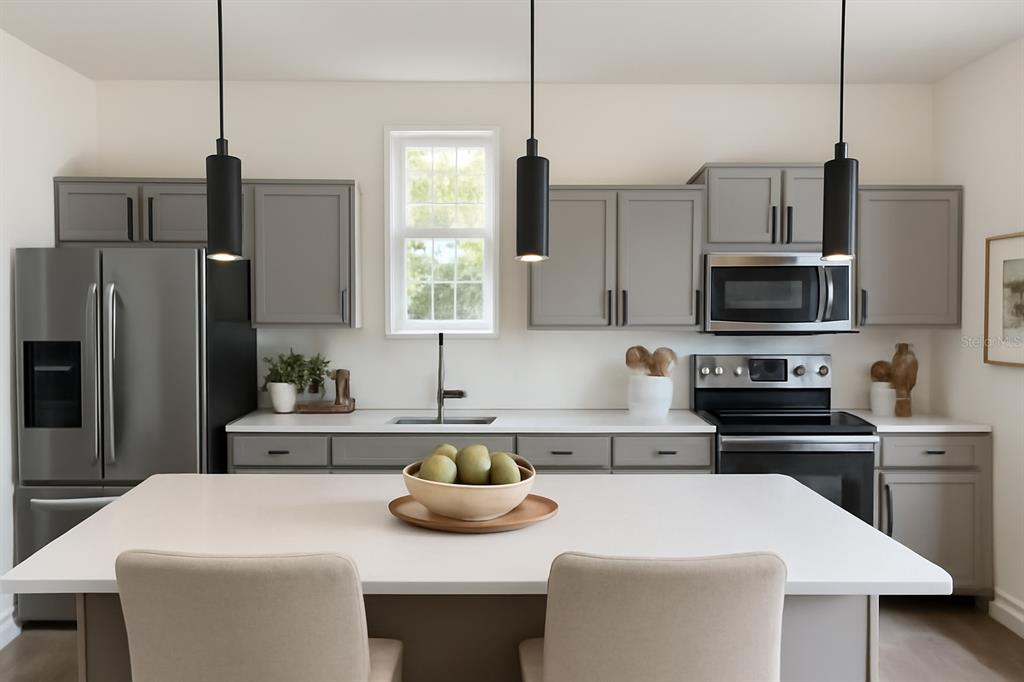 A modern kitchen features gray cabinets, stainless steel appliances, a white island, and pendant lighting — 225 GARDENIA AVENUE, GEORGETOWN, FL