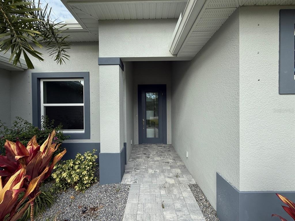 A paved walkway leads to the front entrance of a house with gray stucco walls — 14396 & 14422 CHAMBERLAIN BOULEVARD, PORT CHARLOTTE, FL