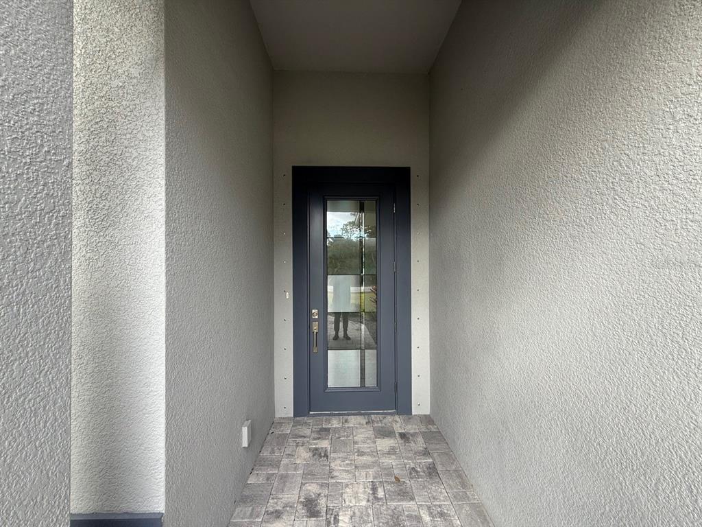A dark gray front door with a glass panel sits in a covered entryway — 14396 & 14422 CHAMBERLAIN BOULEVARD, PORT CHARLOTTE, FL