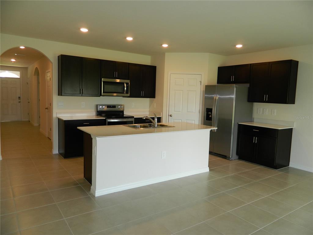 A kitchen features dark wood cabinets, stainless steel appliances, a white island, and tile flooring — 25118 DOREDO DRIVE, PUNTA GORDA, FL