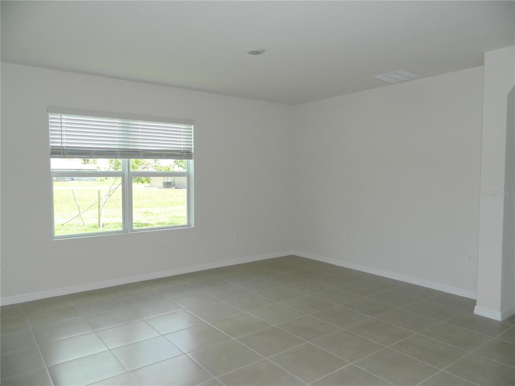 An empty room with white walls, light-colored tile flooring, and a window with blinds — 25118 DOREDO DRIVE, PUNTA GORDA, FL
