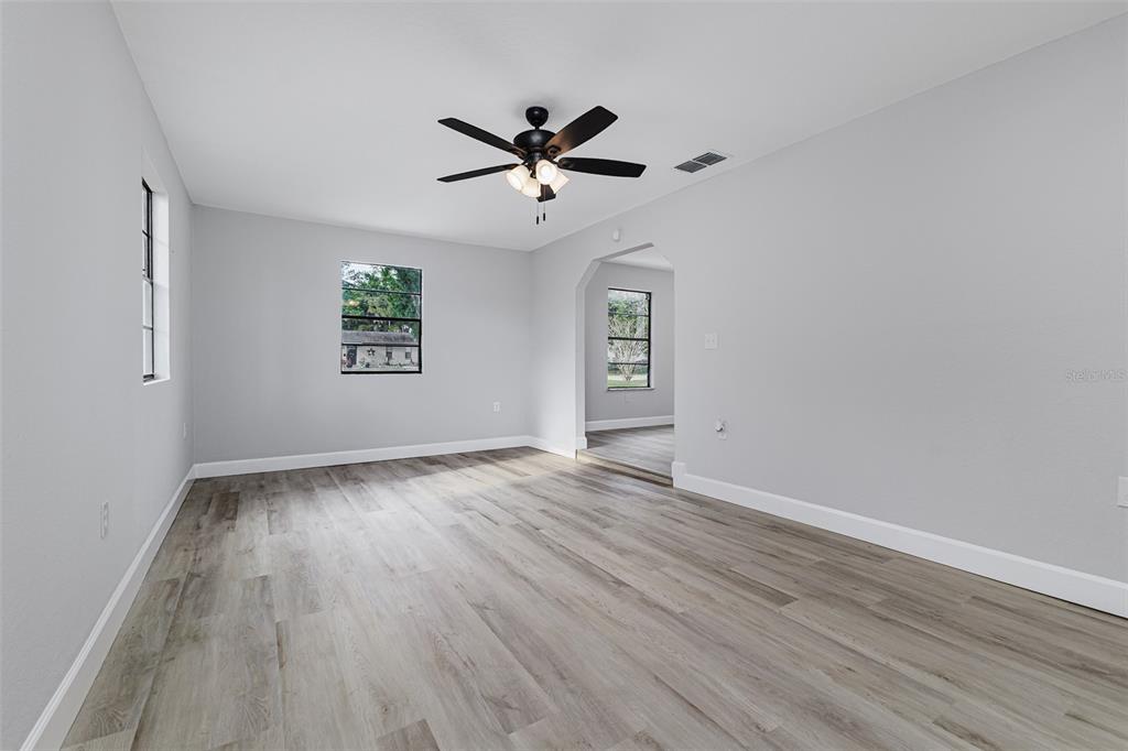 An empty room features light gray walls, wood-look flooring, a ceiling fan, and arched doorways — 4132 CHOWEN DRIVE, LAKELAND, FL