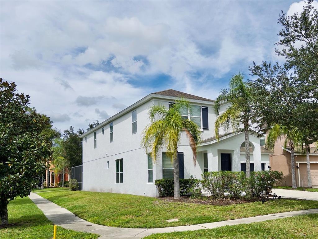 A two-story white stucco house with a palm tree and a sidewalk in the foreground — 210 LAS FUENTES DRIVE, KISSIMMEE, FL