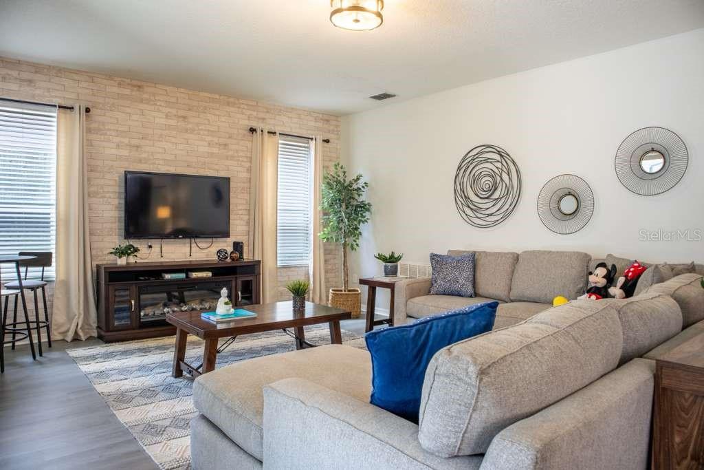 A living room features a faux brick accent wall, a sectional sofa, and wall decor — 210 LAS FUENTES DRIVE, KISSIMMEE, FL