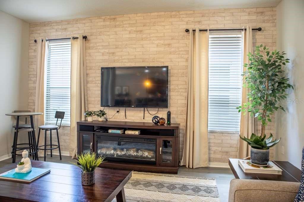 A living room features a faux brick accent wall, a television, and a fireplace console — 210 LAS FUENTES DRIVE, KISSIMMEE, FL