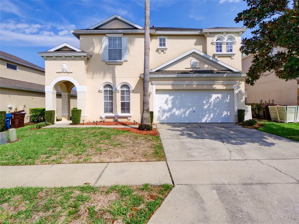 A two-story beige house with a two-car garage, arched windows, and a palm tree — 509 PINELOCH DRIVE, HAINES CITY, FL