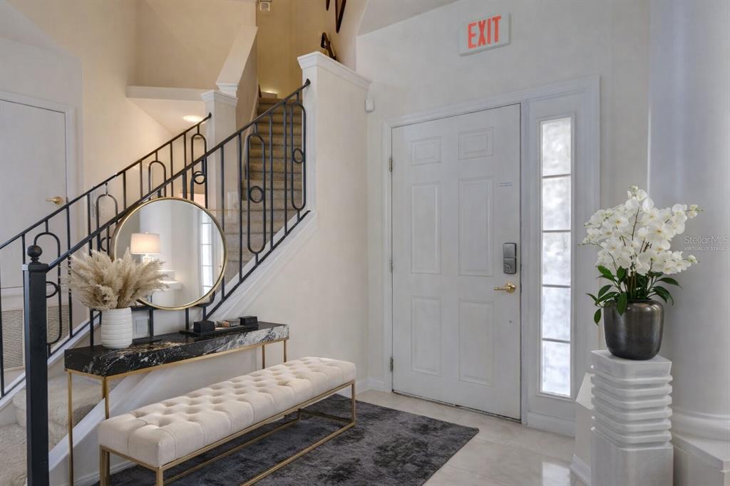 A bright foyer features a staircase with black railings, a tufted bench, and an exit sign — 509 PINELOCH DRIVE, HAINES CITY, FL