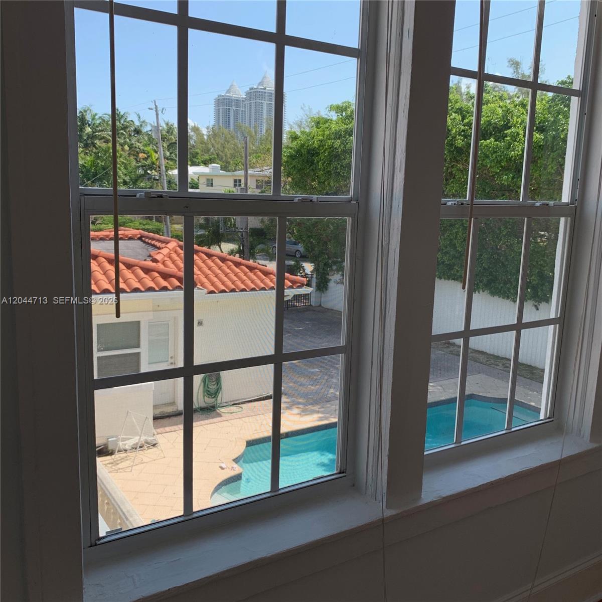 A view through a window shows a backyard with a swimming pool and a building — 4349 Sheridan Ave # 8, Miami Beach FL 33140, MIAMI BEACH, FL