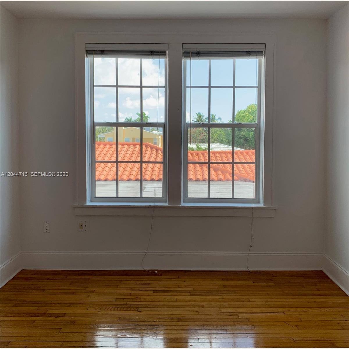 A room with hardwood floors and two windows overlooking a roof with orange tiles — 4349 Sheridan Ave # 8, Miami Beach FL 33140, MIAMI BEACH, FL