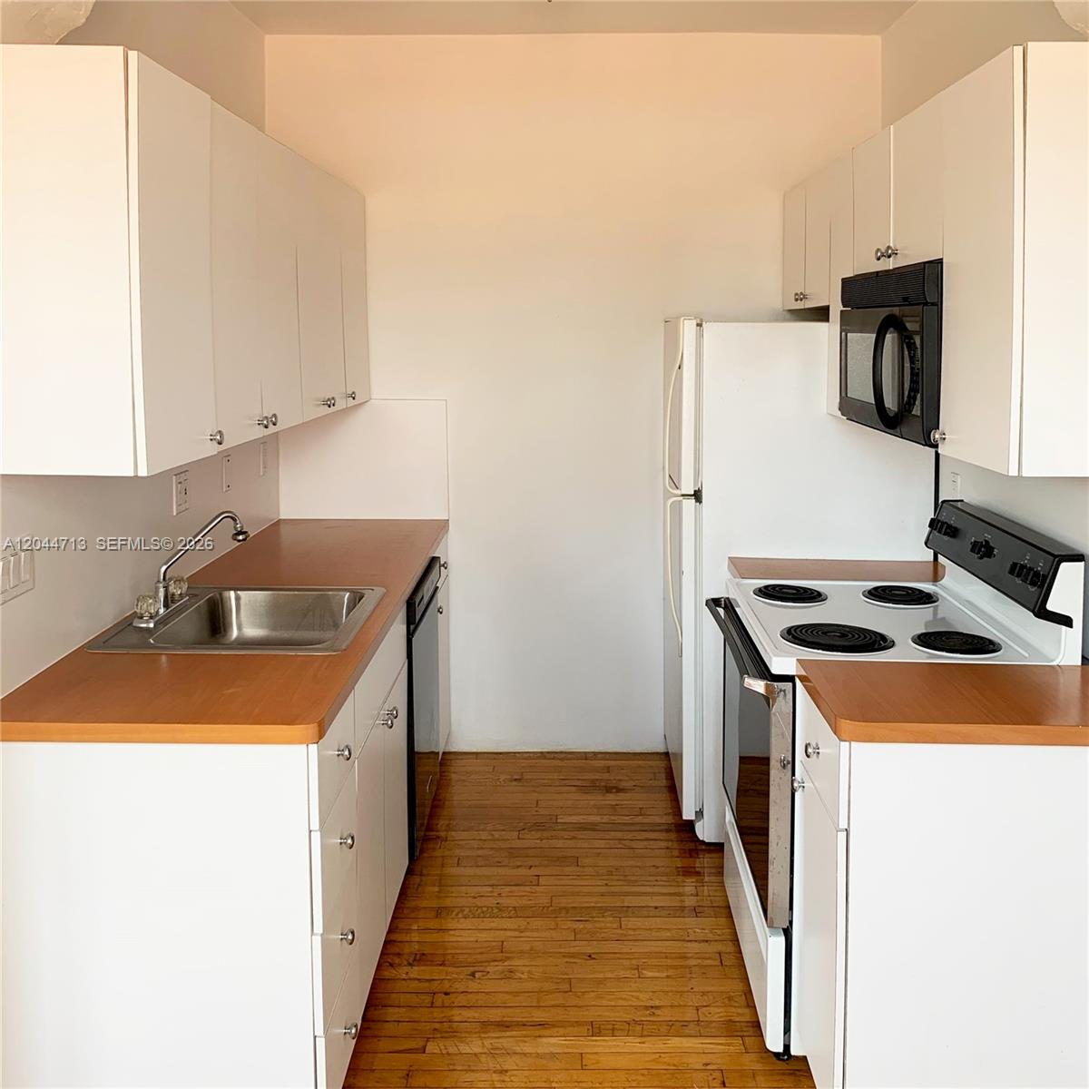 A galley kitchen features white cabinets, wood countertops, a stainless steel sink, and white appliances — 4349 Sheridan Ave # 8, Miami Beach FL 33140, MIAMI BEACH, FL