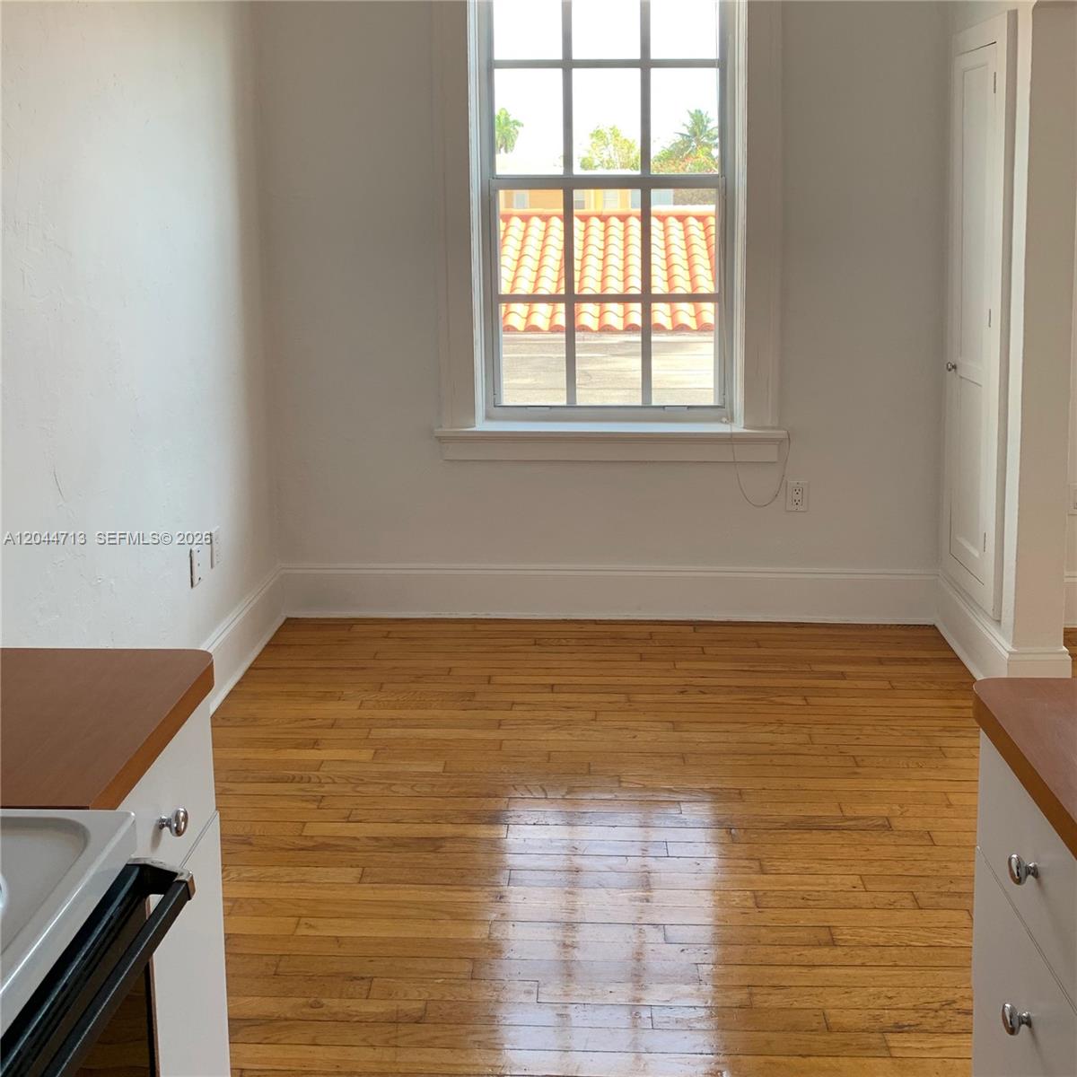 A kitchen area features hardwood flooring, white walls, a window, and white cabinetry — 4349 Sheridan Ave # 8, Miami Beach FL 33140, MIAMI BEACH, FL